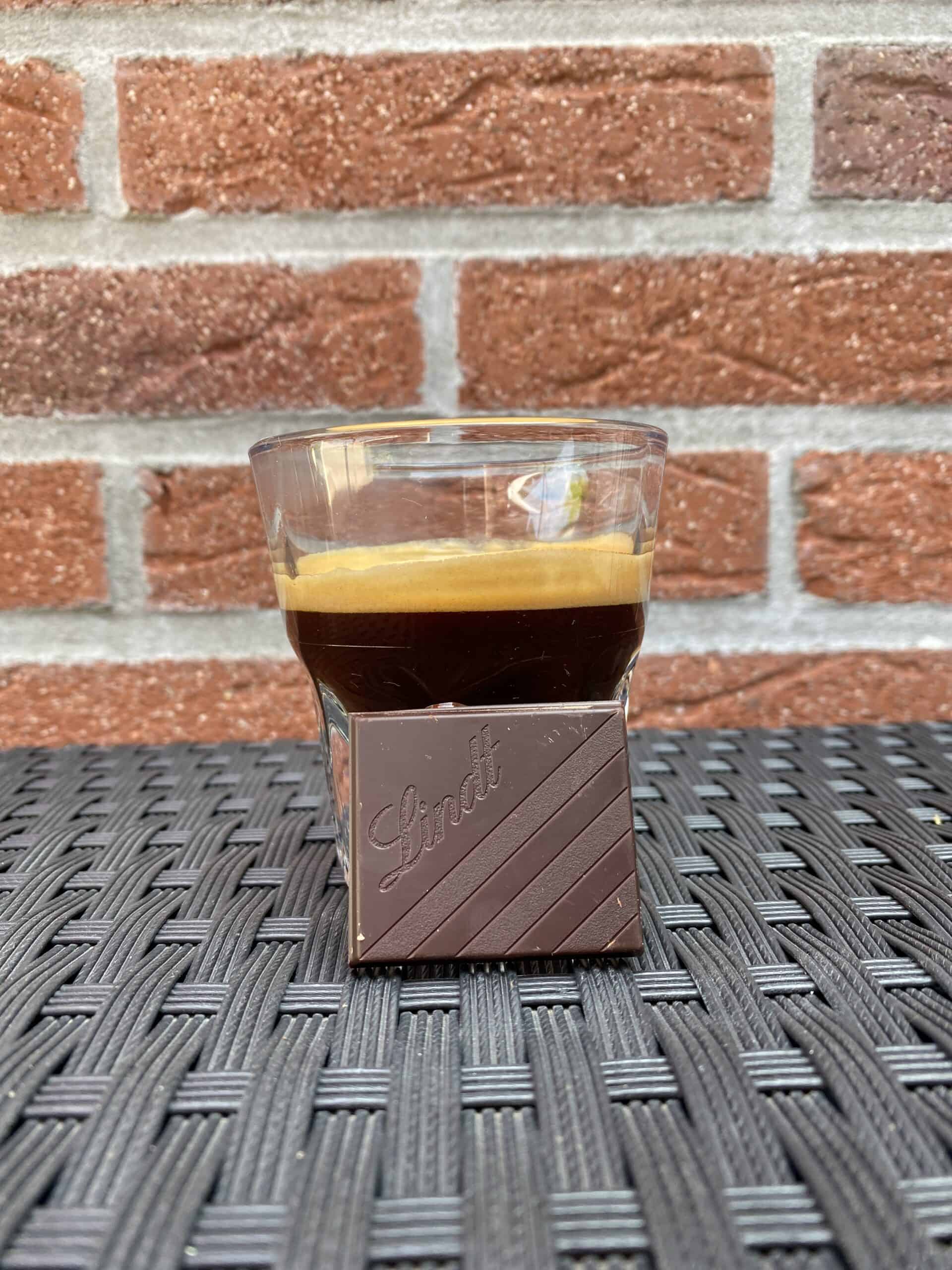 An espresso shot with a square of Lindt dark chocolate in front.