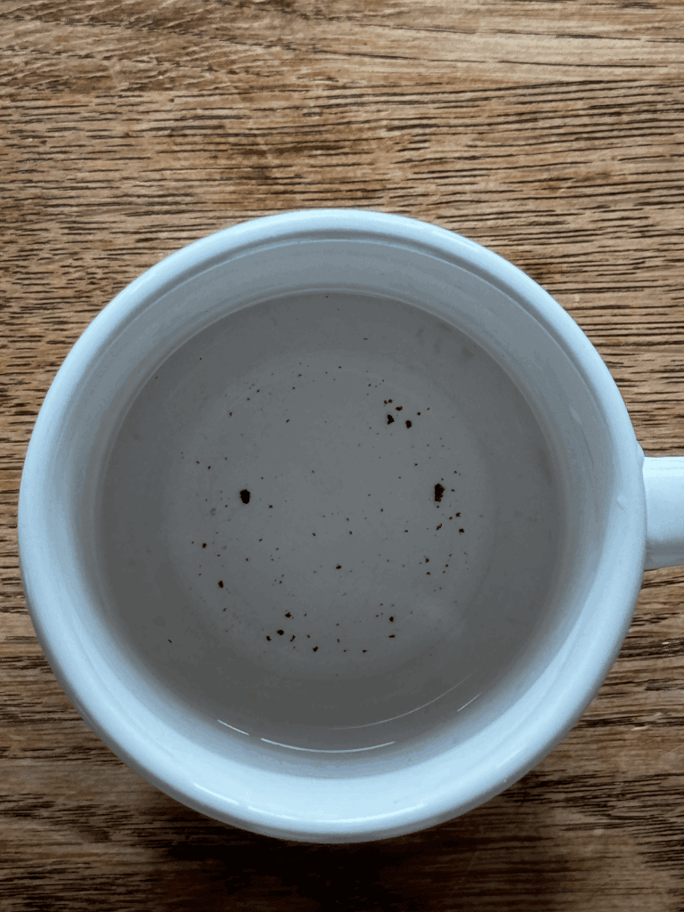 A Nespresso brewed water cup with black specks inside.